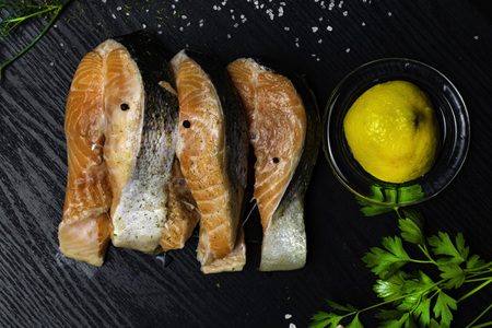 Slices of red fish salmon on trout with lemon in glass, parsley, dill, salt, pepper, selery greens...