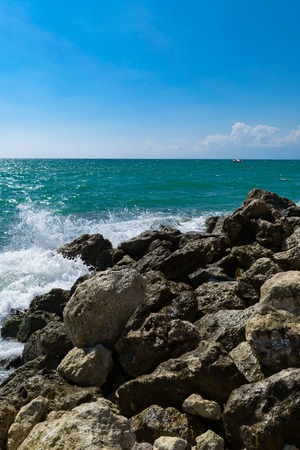 Big stones in clear ocean water on the beach. Shallow ripple water surface.Big Rocks and Stones on Beach.Relaxation Landscape Viewpoint on Daylight Concept Background. Yacht awayの写真素材
