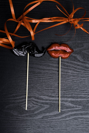 close up of mustache and female red lips made candy, decorated with red ribbon on black wooden background, weeding and love conceptの写真素材