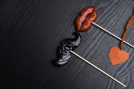 black moustache and a red lips on wooden sticks, decorated with thread, heart, against a split black background copy space for your text as the male and female conceptの写真素材