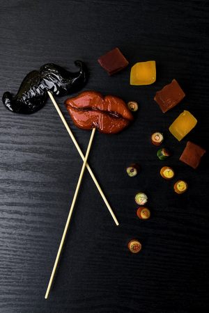 Prop mustache and lips, color candy, marmalade. Creative and colorful gift on wooden dark backgroundの写真素材