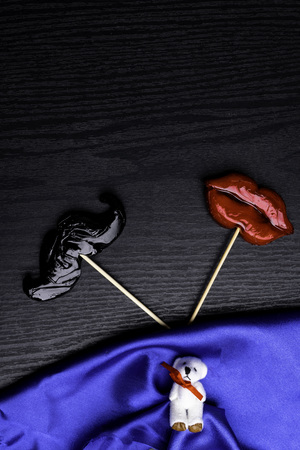 close up of mustache and female red lips made candy, decorated with baby bear toy on black wooden background, weeding and love concept, family conceptの写真素材
