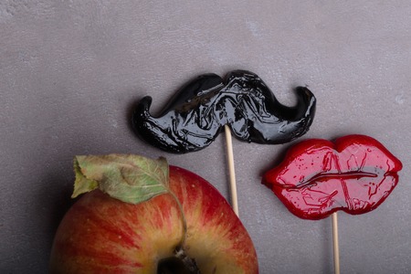 concept of love - mustache and lips icons together is love, simple formula of love and passion between a man and a woman, Forbidden fruit, Adam and Eva concept. Natural hunger and harvest, healthy snack. Red apple and vegetarian or vegan lifestyle. Vitamins from food. The temptation and relationship between man and womanの写真素材