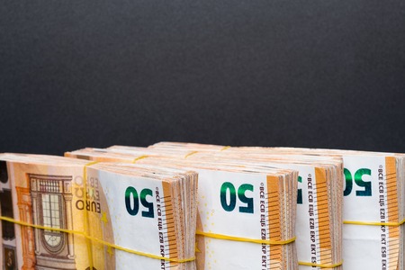 Pile of 50 real euro notes 50-euro banknotes under rubber band, isolated on black background. About...