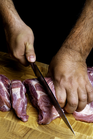 professional man's hands cutting raw pork meat on wooden board, selective focus, close-upの写真素材
