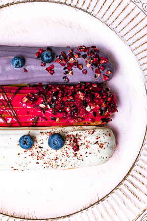 colorful eclairs red white violet with blueberry, raspberry, isolated on white background