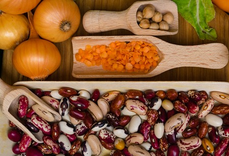 onion, green leafs, beans, lentils, chickpea in wooden spoons on wood background. Organic food....