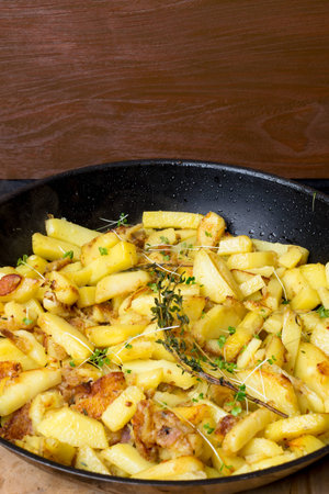 Fried potatoes with green sprouts, rosemary in a cast iron frying pan on wooden background close-upの写真素材