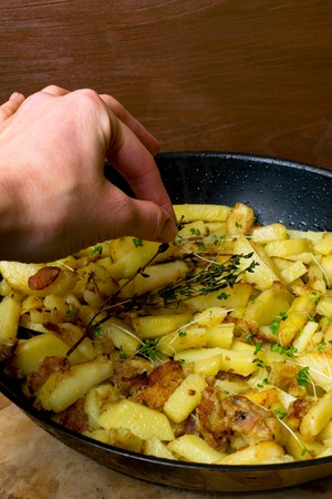 fried potato on pan with green sprouts women hand put branch of rosemary on sliced potatoesの写真素材