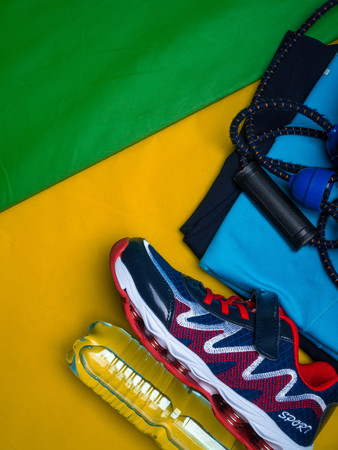 Creative flat lay of sport and fitness equipments clothes, shoe, water, expander on yellow green sport mat background with copy spaceの写真素材