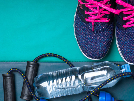 sport set with women sneakers, expander, bottle of water on green mat