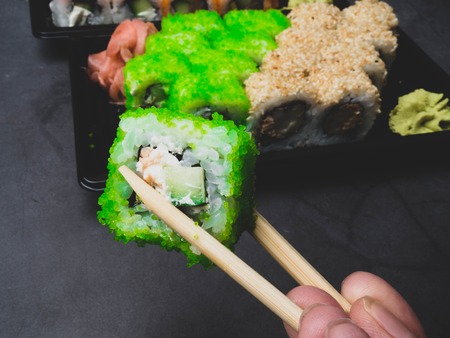 tasty sushi bar, Eating Sushi with chopsticks. Sushi roll japanese food in restaurant. California Sushi roll set with salmon, vegetables, fish, caviar closeup. Japan restaurant menu, selective focus