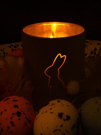 Easter decoration decorative bunny figure on burning at night candle, card with greeting Happy Easter on grey background.の写真素材