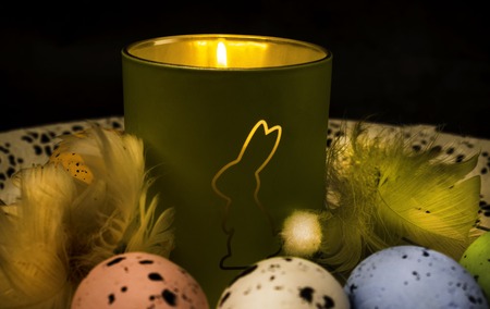 Easter decoration decorative bunny figure on burning at night candle, card with greeting Happy Easter on grey background.の写真素材