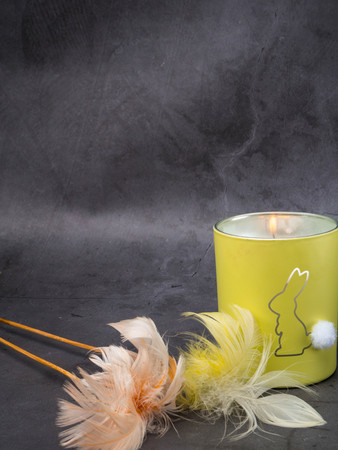 burning candle covered with colorful feathers on concrete background. Decoration, greeting card , postcard, copy spaceの写真素材