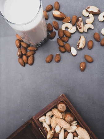 Vegan milk from nuts in glass jar with various nuts on grey background, nuts in wooden box, copy spaceの写真素材
