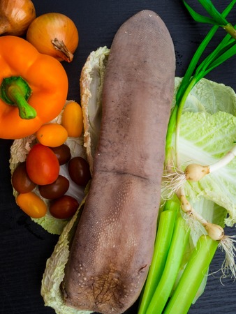 Beef or pork tongue on a board with onions, lettuce leaves, tomatoes, bell pepper,selery, close upの写真素材