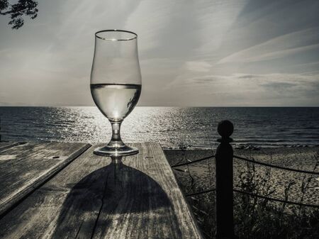 Romantic evening sunset with misty glass of white wine on  sea, on wooden table, copy spaceの写真素材
