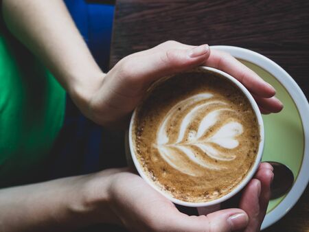 Close up of beautiful female hands holding big white cup of cappuccino coffee. Toned.の写真素材