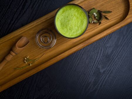 glass of hot matcha coffee latte, whisk, flowers and green matcha powdre on wooden background. Beautiful foam, place for text.の写真素材