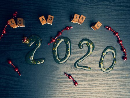 Loading for new 2020 year on wooden board, with text inscription, red garland, copy space