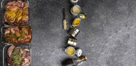 Marinating raw meat in different spices, herbs and marinades, with soy sauce and oil on grey...