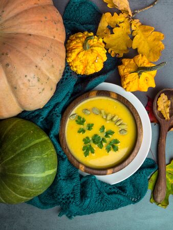 Vegetarian autumn pumpkin cream soup with seeds, parsley, in wooden bowl, with with autumn leaves and decorative pumpkins, soft plaid Top viewの写真素材