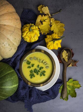 Vegetarian autumn pumpkin cream soup with seeds, parsley, in wooden bowl, with with autumn leaves and decorative pumpkins, soft plaid Top viewの写真素材
