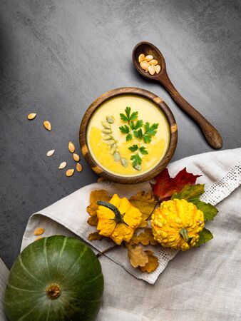 hot yellow pumpkin and lentils soup, with seeds, parsley in oak wooden bowl, spoon from wood, decorative autumn foliage on kitchen linen towel, Vegetarian autumn soupの写真素材