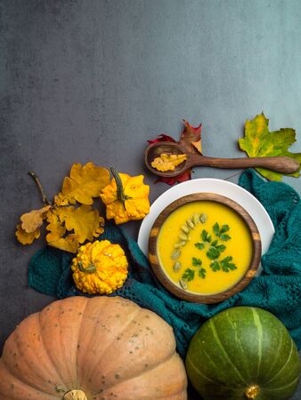 Vegetarian autumn pumpkin cream soup with seeds, parsley, in wooden bowl, with with autumn leaves and decorative pumpkins, soft plaid Top viewの写真素材
