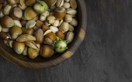 Various nuts in wooden bowls on dark wooden background . Almonds , pistachios, hazelnut and pumpkin...