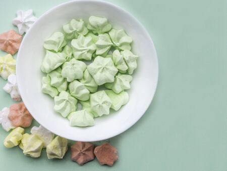 Mint, coral color, and yellow meringues on pastel green table. Many trendy top view dessert image....