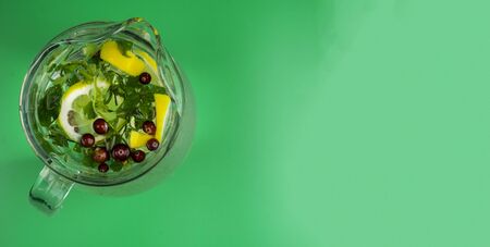 Refreshing drink with lemon lime cranberries mint in glass jars on trendy mint green color background Healthy detox drink.の写真素材