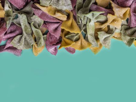 Pile of Italian dried Tri Color Farfalle pasta. Various colors of bow tie on trendy green mint color backgroundの写真素材