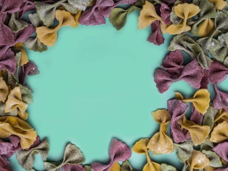 Pile of Italian dried Tri Color Farfalle pasta. Various colors of bow tie on trendy green mint color backgroundの写真素材