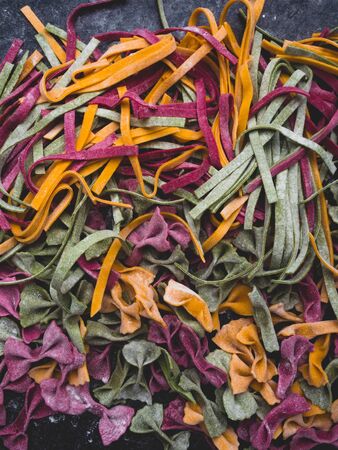 Homemade pasta, farfalle bow-tie, fettuccine or tagliatelle colorful pasta on grey background with...