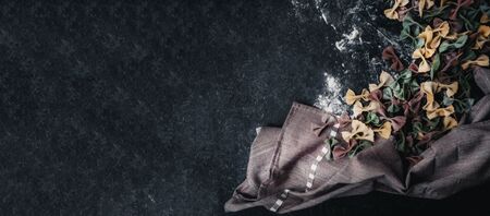 Homemade colorful Italian pasta on grey marble background. Various colors of bow tie tagliatelle, farfalle with flour, kitchen towel. Top view. Selecive focus., copy spaceの写真素材