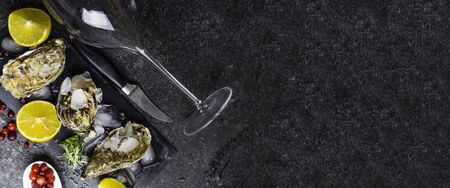 Fresh oysters in ice with lemon, cranberries, glass for wine or champagne, knife over stone table,...
