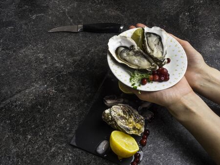 Open oyster in women hands, against a background of open oysters, selective focus