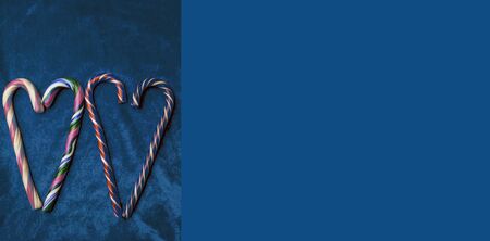 Holiday candy canes heart on trendy blue background with copy space, top view