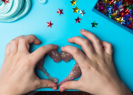 Heart shape glitter slime with colorful stars on a blue table, children trendy toyの写真素材