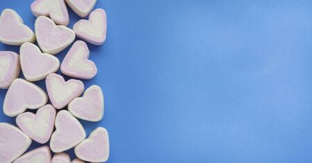 Pink marshmallow in heart shape stacked on trendy blue background with copy space. Sweet candy for...