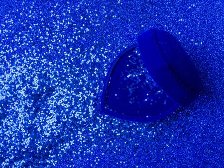 Blue velvet heart shaped ring box with glitters on trendy blue background. Gift for valentines day or birthday. Copy space for text, symbols of february romantic holiday or wedding designの写真素材