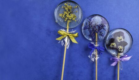 Round lollipop with blue cornflower, pansies, elder decorated with bows, on trendy blue classic background, flat lay minimal concept, trendy pop art style photo, isolatedの写真素材