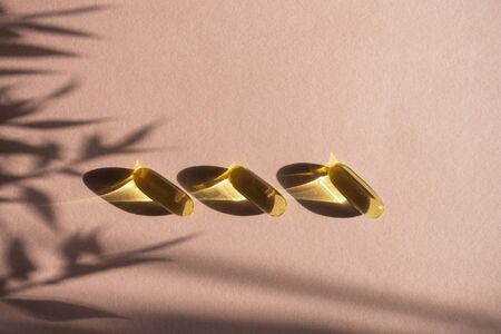 Oil yellow gelatin capsules on pink background with flower shadow, vitamins and antioxidant concept...