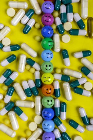Multi color pills, tablets and capsules with colorful funny faces with emotions on yellow background. Medicine concept. Healing. Antidepressant pills. Close upの写真素材