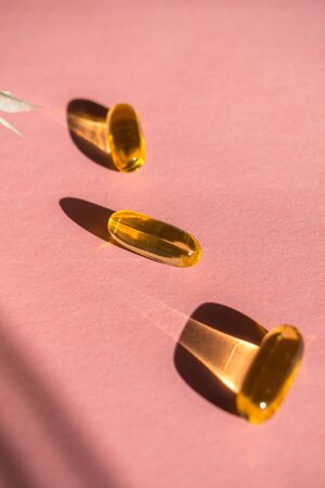 Oil yellow capsules on pink background, vitamins and antioxidant concept Omega 3, liver cod or evening primose oil for healthcare. Trendy shadow, selective focusの写真素材