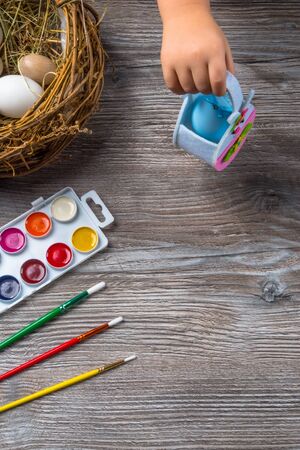 easter eggs in nest and colorful paints and brushes on wooden background. Baby beginning to painting. Close upの写真素材