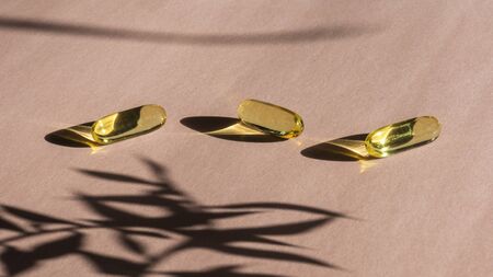 Oil yellow gelatin capsules on pink background with flower shadow, vitamins and antioxidant concept...