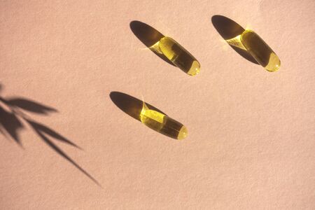 Oil yellow gelatin capsules on pink background with flower shadow, vitamins and antioxidant concept...